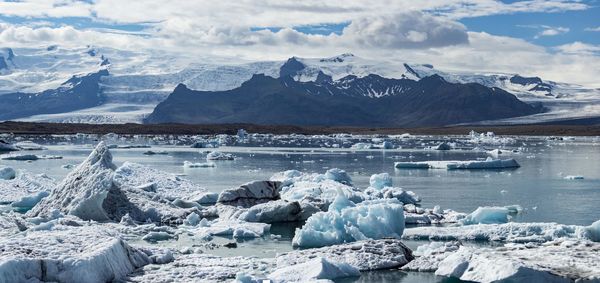 Ice floating in sea by snowcapped mountain against sky