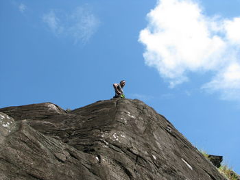 Low angle view of man climbing on mountain against sky