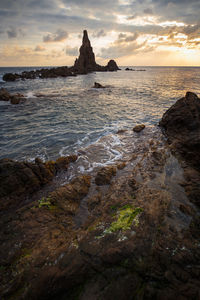 Rock formation at beach against cloudy sky during sunset