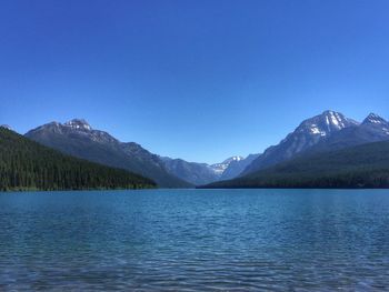 Scenic view of lake by mountains against clear blue sky