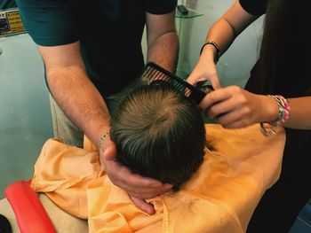 Midsection of father holding son having haircut by hairdresser in barber shop