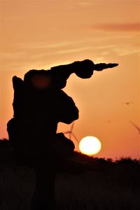 Silhouette sculpture on field against sky during sunset