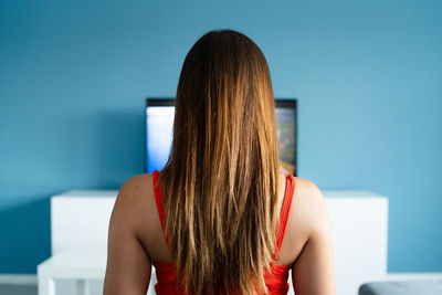 Rear view of woman watching tv while sitting on sofa at home