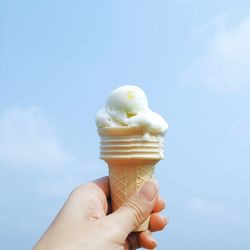 Cropped woman holding ice cream cone against sky