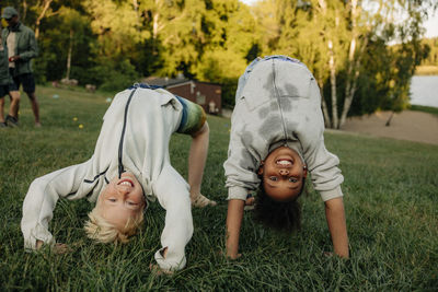 Portrait of playful male and female friends doing bridge position on grass in playground