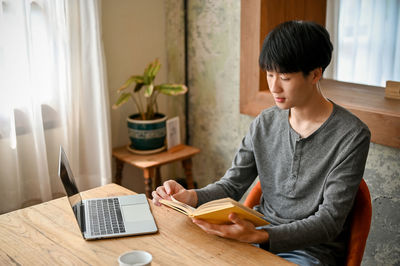 Side view of young woman using digital tablet while sitting at home