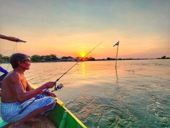 Man fishing in sea against sky during sunset