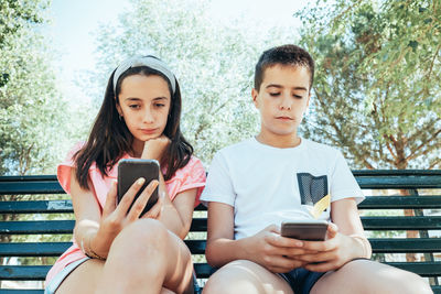 Siblings using phones while sitting on bench