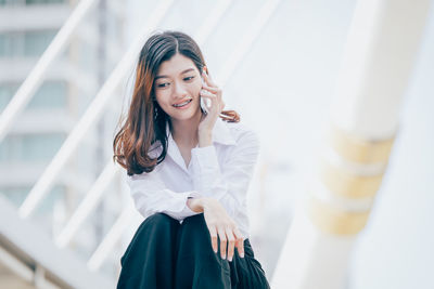 Low angle view of young woman using mobile phone while sitting outdoors