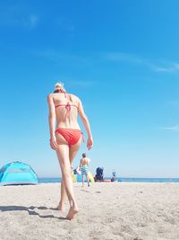 Rear view of bikini woman walking at beach against sky