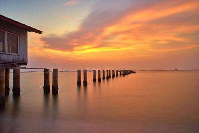 Wooden posts in sea against orange sky