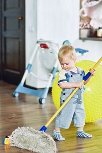 Full length of boy cleaning floor with mop at home