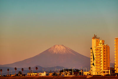 Cityscape and snowapped mountain against sky during sunrise