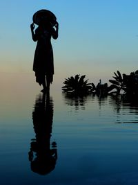Silhouette woman standing at shore against sky during sunset