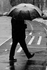 Low section of man with umbrella walking on wet street