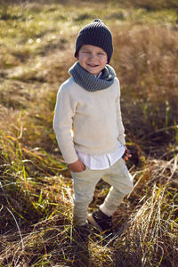 Boy in warm clothes stand along a path on a field with dried grass in autumn