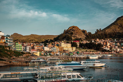 Sailboats moored in harbor by town against sky