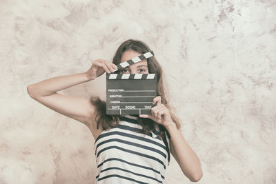 Portrait of young woman holding film slate by wall