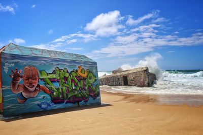 Graffiti on beach by sea against sky