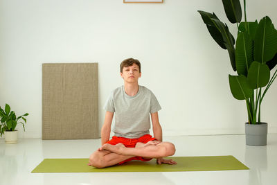 A teen boys sit in the lotus position, in a bright room