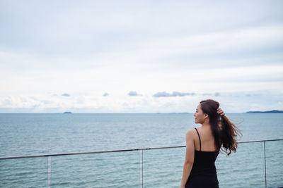 Rear view image of a beautiful young asian woman standing and looking at the sea and blue sky