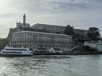 View of buildings by river against cloudy sky