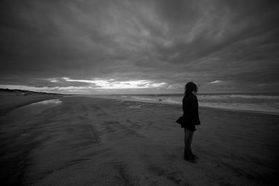 Woman standing on beach against sky during sunset