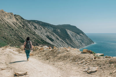 Rear view of man walking on mountain against sky