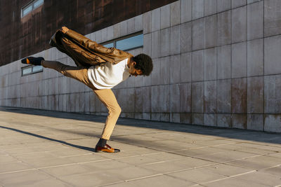 Male dancer dancing on one leg against building