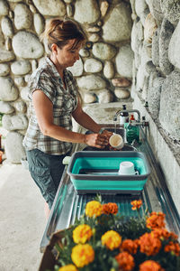 Woman washing up the dishes pots and plates in the outdoor kitchen during vacations on camping