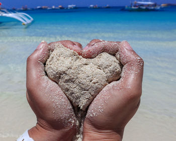 Midsection of person holding heart shape on beach