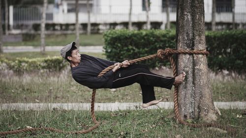 Full length of man climbing on tree trunk in field