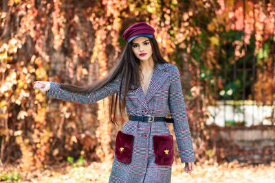 Fashionable young woman standing against plants during autumn