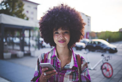 Portrait of confident young woman with afro hairdo in the city at dusk