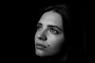 Close-up of young woman looking away against black background