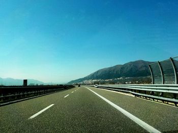 Road leading towards mountains against clear blue sky