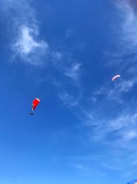 Low angle view of people paragliding against blue sky