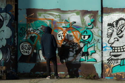 Full length of young woman standing against graffiti wall