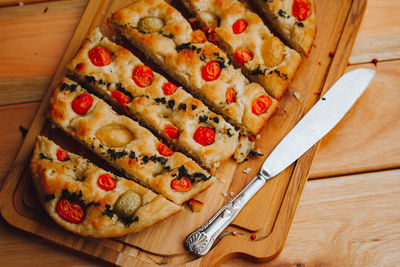 Homemade italian focaccia cut into slices, with tomato and olive oil on a rustic wooden background.