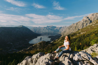 Woman sitting on rock by lake against sky