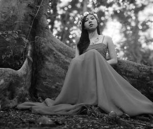 Low angle view of woman in evening gown sitting by tree trunk