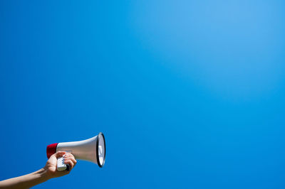 Midsection of woman holding umbrella against blue sky