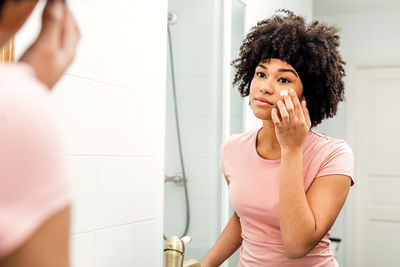 Teenage girl applying moisturizer in front of mirror at bathroom