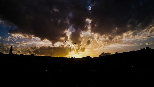 Silhouette birds on landscape against dramatic sky