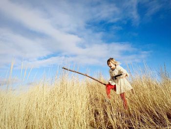 Happy girl with stick walking on field against sky