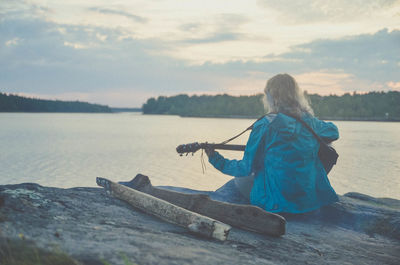 Rear view of woman sitting by sea against sky