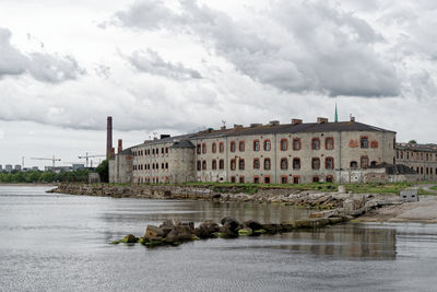 Buildings by river against cloudy sky