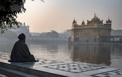 Man looking at golden temple against sky during sunrise