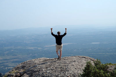 Rear view of man standing on rock against sky