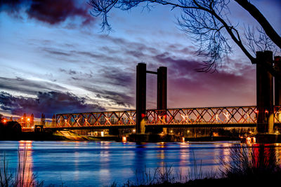 Illuminated bridge over river against sky at sunset